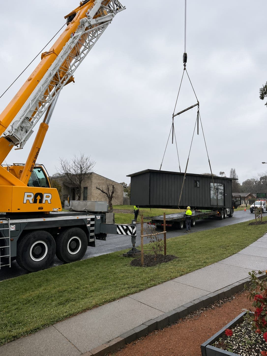 A Modlux modular home being lifted from a transport trailer by crane on a suburban street