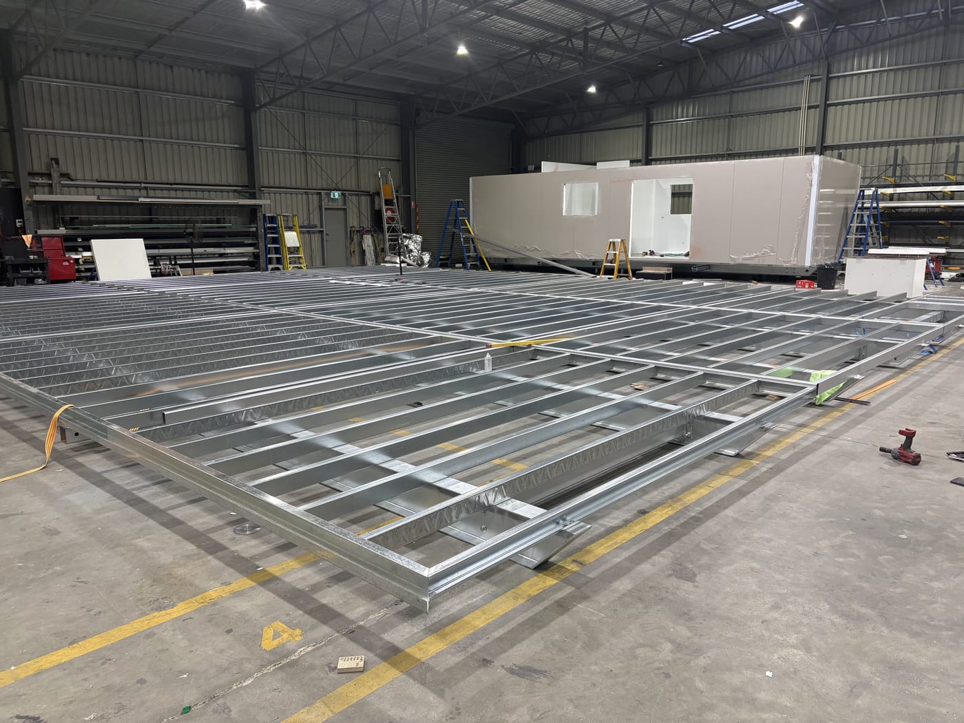 A completed steel floor chassis squared up in the Modlux factory, with a finished module behind it