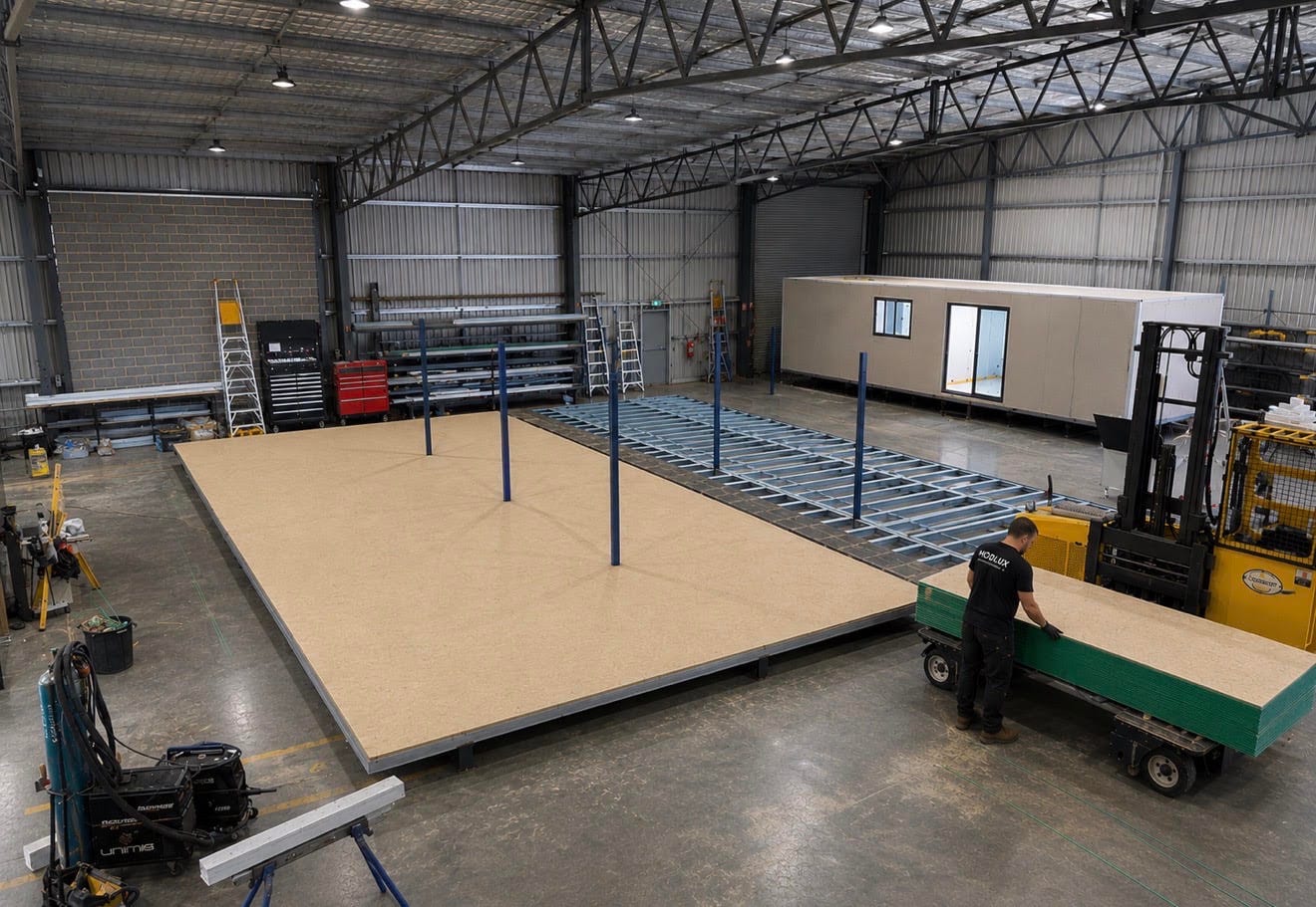 The Modlux factory floor: a subfloor being laid over a steel chassis, with a finished module in the background